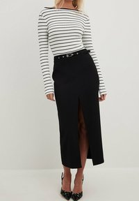 Svart pennkjol med en framfick, kombinerad med en vit randig långärmad topp. Outfiten har ett svart bälte med en silverfärgad spänne.