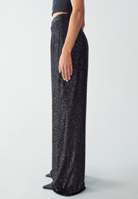 Pantaloni larghi neri con paillettes e vita alta, caratterizzati da righe verticali e una texture liscia, abbinati a décolleté nere appuntite.