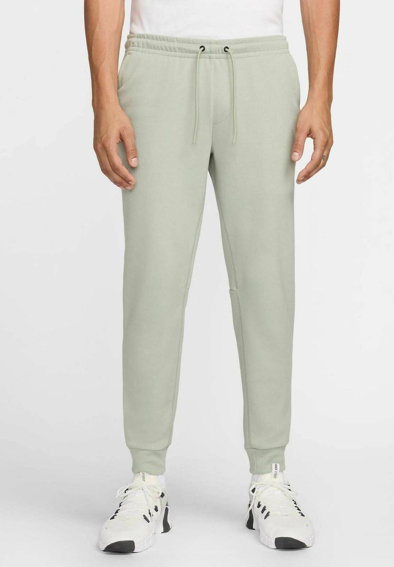 Light green sweatpants with an elastic waistband and drawstring, featuring side pockets and tapered cuffs, paired with white sneakers.