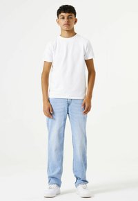 Camiseta blanca de manga corta combinada con jeans rectos de tiro medio azul claro, llevada con zapatillas blancas sobre un fondo liso.