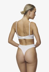 Bralette blanche avec des bretelles réglables et un fermoir au dos, associée à un string taille haute blanc. Tissu lisse, design minimal, sans motifs ni embellissements.