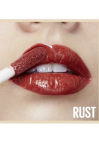 Glossy, couleur rouille profonde de gloss à lèvres appliqué sur des lèvres pulpeuses, avec un applicateur doux à bout texturé. Fini lisse et réfléchissant.