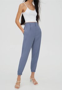 Ljusblå tapered byxor med elastiska mudd, veckad front, sidofickor och hög midja, parat med en vit linne och sandaler med remmar.