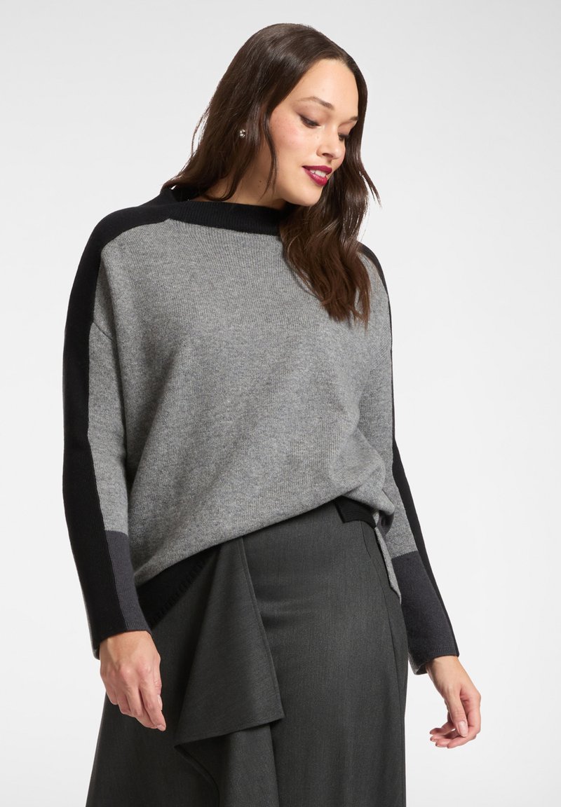 Übergroßer Pullover in Grau mit schwarzen Akzenten; lange Ärmel und runder Halsausschnitt; weicher, strukturierter Strickstoff; kombiniert mit einem dunklen Wickelrock.