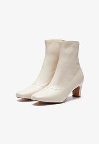 Botas de tobillo blancas hechas de cuero suave, con punta cuadrada y un tacón bajo y ancho. Las costuras realzan el diseño elegante.