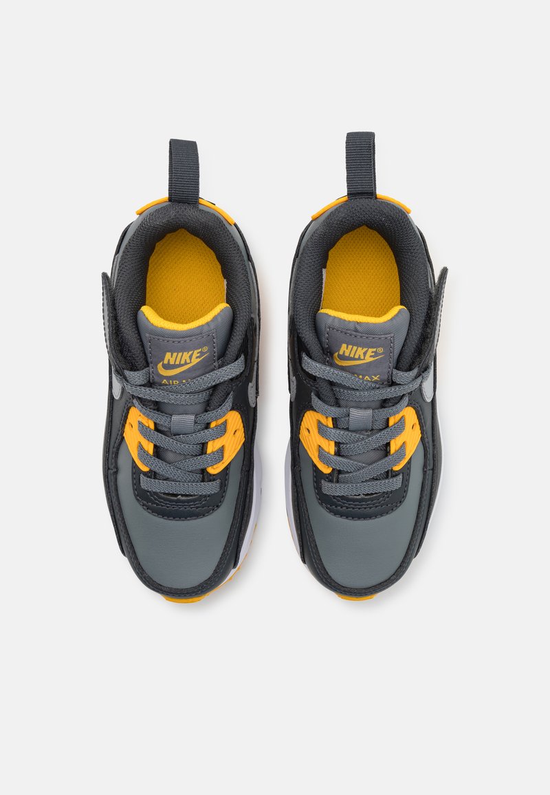 Zapatillas Nike Air Max con parte superior gris, acentos amarillos, cordones grises, lengüeta acolchada y suela de goma. Presentan una superficie texturizada y detalles del logo.