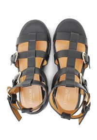 Schwarze Ledersandalen mit mehreren Riemen, einer hellbraunen Innensohle und goldenen Hardware-Akzenten. Flache Sohle mit einer strukturierten Oberfläche.