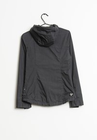 Giacca nera con cappuccio realizzata in materiale leggero. Presenta una cerniera, polsini regolabili e un logo vicino all'orlo. Tessuto testurizzato con un leggero lucido.