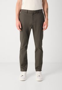 Olijfgroene, op maat gemaakte chino's met een soepele textuur, voorzien van een knoopsluiting, zijzakken en een tapered leg ontwerp, gecombineerd met witte sneakers.