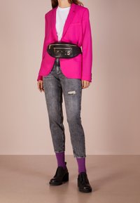 Blazer rosa, camiseta blanca, jeans gris desgastados, calcetines morados, zapatos negros gruesos y una riñonera negra con detalles en oro.