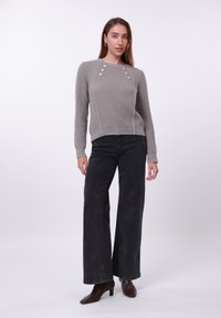 Grå ribbestrikket genser med tre dekorative knapper på skulderen, kombinert med svarte vide jeans og brune ankelstøvletter med hæl.