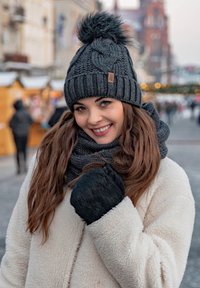 Bonnet en tricot gris avec un pompon, écharpe sombre assortie et mitaines noires. La texture semblable à de la laine offre de la chaleur dans un environnement hivernal.