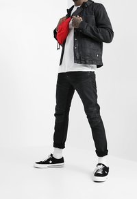 Musta denim-takki, valkoinen t-paita, mustat farkut, joissa on ompelut yksityiskohdat, ja mustat lenkkikot, joissa on valkoisia korostuksia. Päällä punainen olkalaukku.