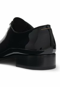 Zwarte gepatineerde leren formele schoenen met een lage gestapelde hak, een gladde glanzende afwerking en een instapontwerp, getoond vanuit een schuin achteraanzicht.