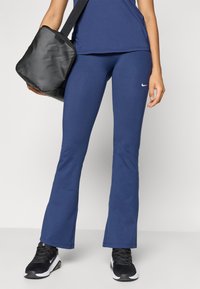 Navyblå, flagrende leggings laget av elastisk stoff, med en liten hvit Nike-logo. Kombinert med svarte treningssko og en svart bag.