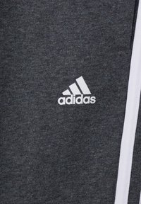 Mörkgrå träningsbyxor i mjukt material. Har vitt adidas-logotyp och vita randdetaljer på sidan.