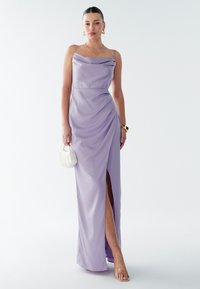 Lavendli satiinist õhtukleit lohvikkaeluse, külje lõhikuga ja drapeeringudetailiga; kombineeritud valge ümmarguse käekoti ja rihmkontsad jalas.