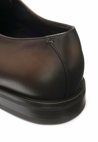 Scarpa in pelle marrone con tacco arrotondato, texture liscia e dettagli di cucitura sottili. Presenta una suola in gomma con un bordo testurizzato per una migliore aderenza.