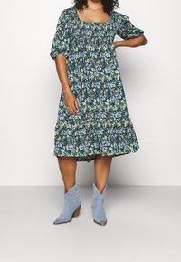 Kukkamekko neliökaula-aukolla, lyhyillä puffihihnoilla ja kerrostetulla hameella sinisen, keltaisen ja vihreän kuvioinnin kanssa. Yhdistetty vaaleansinisiin cowboy-kengiksi.