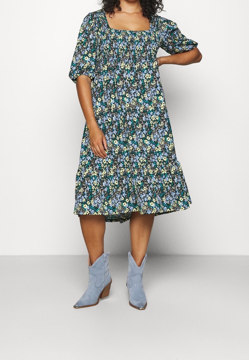 Kukkamekko neliökaula-aukolla, lyhyillä puffihihnoilla ja kerrostetulla hameella sinisen, keltaisen ja vihreän kuvioinnin kanssa. Yhdistetty vaaleansinisiin cowboy-kengiksi.