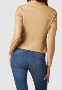 Tanleren jas met een aansluitend ontwerp en een achterpasdetail, gecombineerd met donkerblauwe jeans voorzien van zakken met lapstukken en een taille die tot halverwege de heupen reikt.