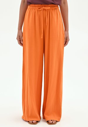 Persona che indossa pantaloni larghi arancioni con vita elastica e coulisse, abbinati a sandali aperti.