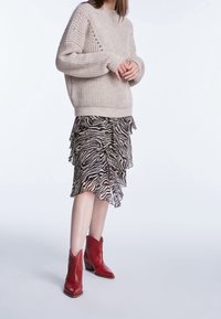 Beige striktrøje med et struktureret design, lagdelt zebra-print nederdel og røde læder ankelstøvler med spidse tæer og blokhæle.