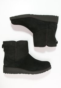 Botines de gamuza negra con suela baja en cuña, que presentan una textura suave y una asa en la parte posterior para facilitar su uso.