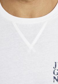 Weißes Baumwoll-T-Shirt mit V-Ausschnitt, strukturiertem Stoff und einem navyblauen Logoaufdruck auf der unteren rechten Seite.