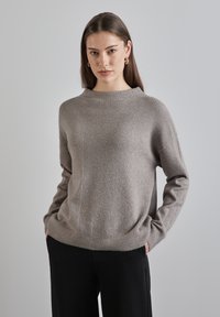 Hellgrauer Strickpullover mit gerippter Textur, hohem Kragen und lockerer Passform. Mit abfallenden Schultern und geradem Saum. Passt gut zu dunklen Hosen.