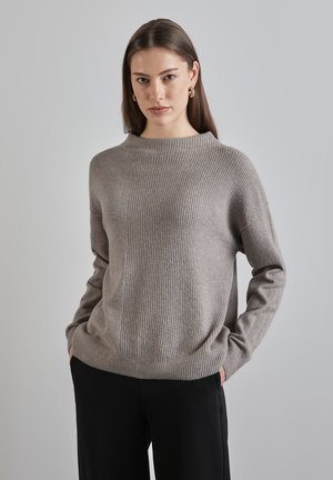 Lys grå strikket sweater med ribbet tekstur, høj hals og afslappet pasform. Har sænkede skuldre og lige kant. Passer godt sammen med mørke bukser.