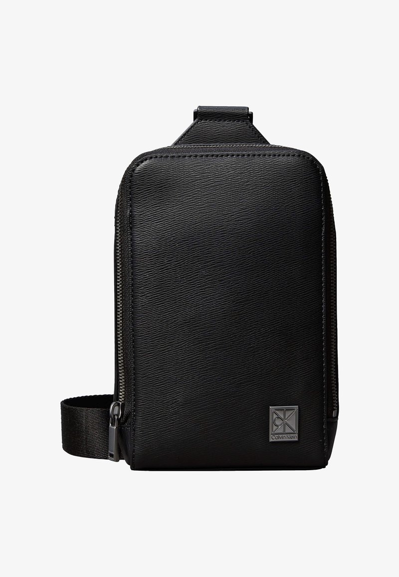 Black textured rectangular sling bag with zipper closure and adjustable strap, featuring a small Calvin Klein metal logo plate.