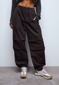 Bruine cargobroek met gelaagd ontwerp, elastische tailleband en zakken. Gecombineerd met beige sneakers met lichte en donkere accenten.
