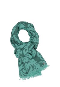Sciarpa teal con motivi floreali scuri, annodata in modo slacciato con bordi frangiati e un piccolo tag metallico rotondo in un angolo.