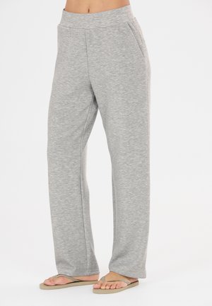 Person iført lysegrå joggingbukser og beige flip-flops, der står mod en ensfarvet hvid baggrund.