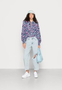 Blusa floral de manga longa com decote em gota, jeans rasgados azul claro, ténis de plataforma brancos e um chapéu de balde brilhante azul claro.