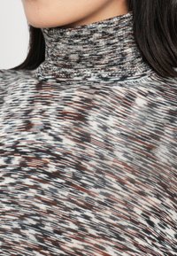 Hladký top s vysokým golierom v zmesi šedých, čiernych a hrdzavých tónov. Tkanina vykazuje textúrované pletenie s horizontálnymi a vertikálnymi pruhmi.
