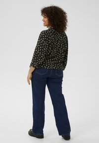 Blouse noire à imprimé floral avec une coupe décontractée, associée à un jean évasé en denim bleu foncé. Tissu texturé et détails de couture simples visibles.