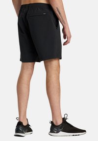 Black shorts with a simple design, elastic waistband, and a back pocket. Worn with black athletic shoes featuring a white sole.