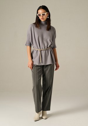 Top grigio lavorato a maglia con maniche corte e collo alto, cintato in vita con una cintura beige, abbinato a pantaloni grigi a righe sottili e tacchi bianchi.