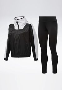 Veste de sport zippée noir et blanc avec col montant associée à des leggings noirs taille haute et longueur intégrale sur fond blanc.