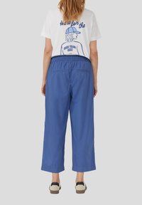 T-shirt bianca con design grafico blu, abbinata a pantaloni blu larghi, che arrivano a metà polpaccio, con cintura elastica e due tasche posteriori.