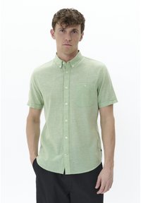 Camicia a maniche corte, verde chiaro, con bottoni, realizzata in un tessuto texture, colletto, taschino sul petto e orlo curvato. Sono visibili dettagli in contrasto sui bottoni.