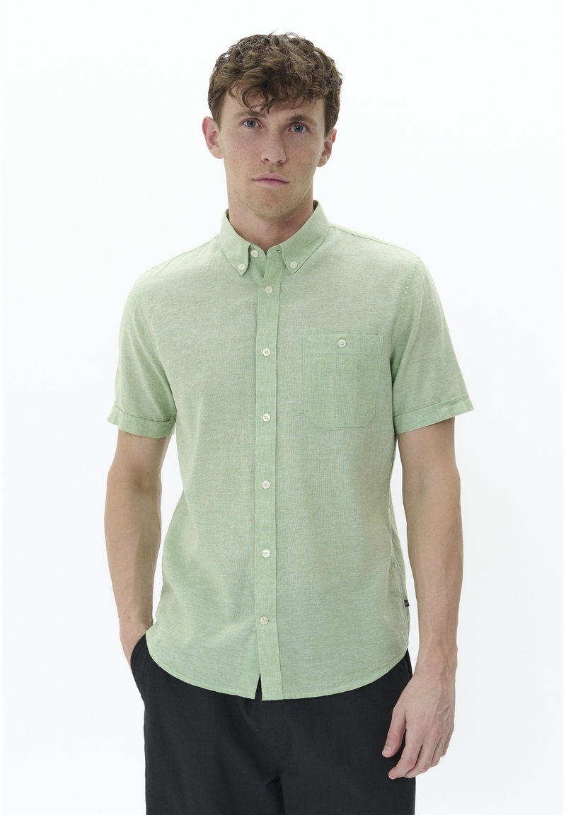 Camicia a maniche corte, verde chiaro, con bottoni, realizzata in un tessuto texture, colletto, taschino sul petto e orlo curvato. Sono visibili dettagli in contrasto sui bottoni.