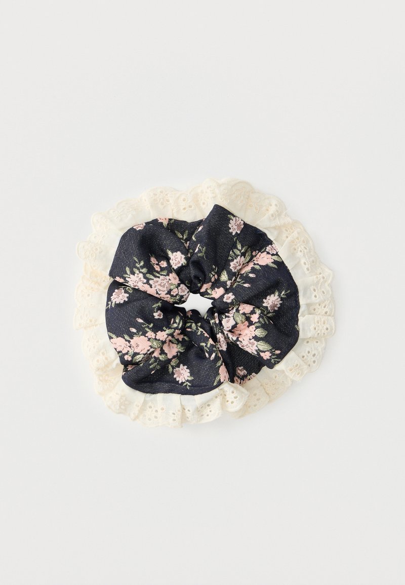 Čierna látková scrunchie s ružovo-zeleným kvetinovým vzorom, obklopená krémovou čipkou s očkami, na bielom pozadí.