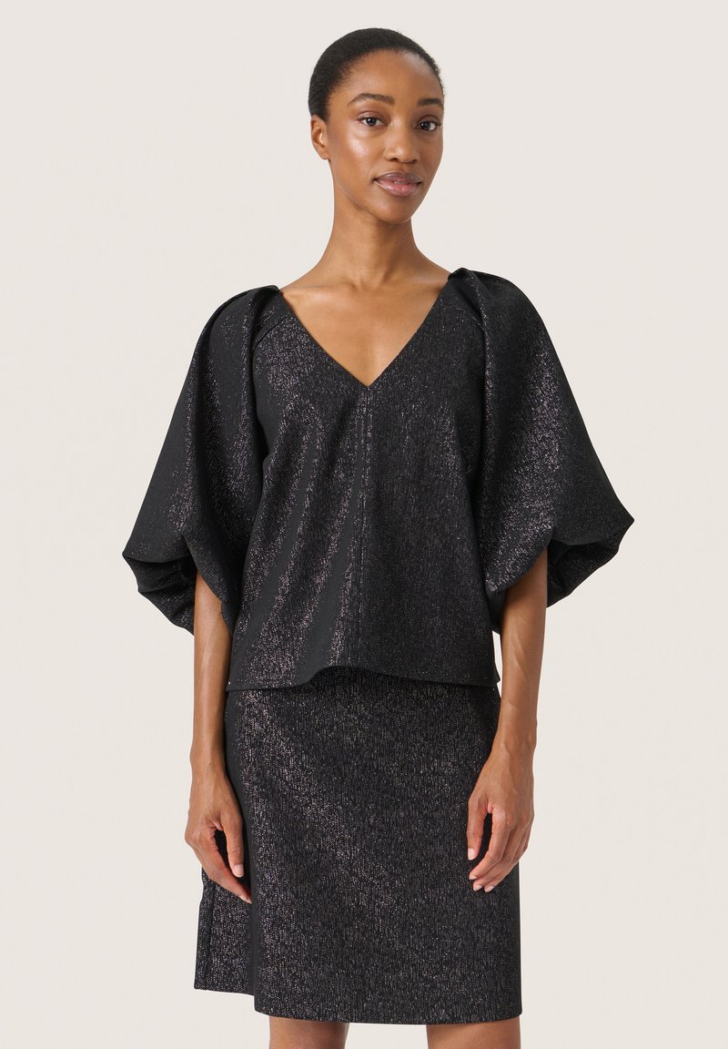 Top nero con scollo a V, maniche larghe e una texture luminosa, abbinato a una gonna a tubino coordinata. Entrambi i capi presentano una silhouette snella e aderente.
