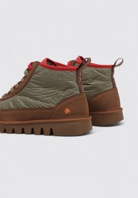 Zapatos de ante marrón de corte medio con parte superior acolchada verde, forro rojo y una suela de goma texturizada con un logotipo de estrella naranja.