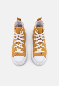High-top sneakers in mustard yellow canvas with white laces and rubber soles. Features a pull tab at the heel and a smooth texture.