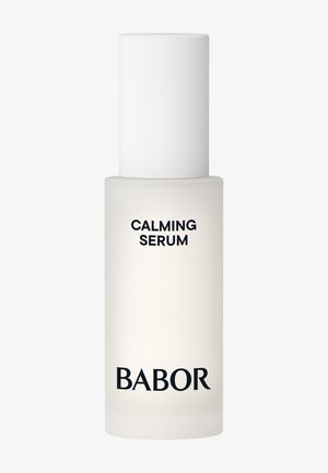 Klar glasflaska med frostad yta, vit kapsyl. Etiketten säger "CALMING SERUM" och "BABOR" i svart text. Slät yta och cylindrisk form.