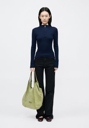 Top a maniche lunghe a coste blu navy con mezza zip, abbinato a jeans neri svasati e una borsa tote in pelle scamosciata verde tenue. Scarpe slip-on bordeaux scuro.